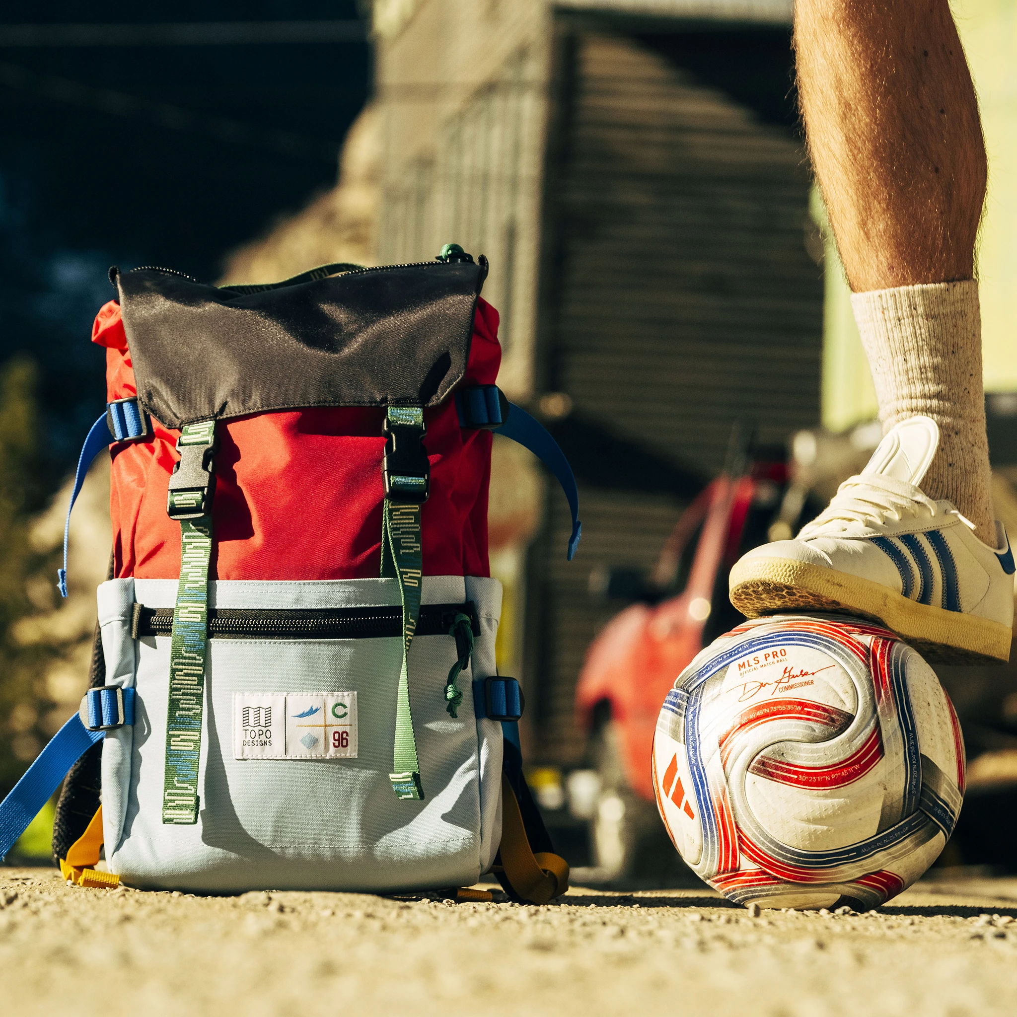 A red and gray backpack beside a soccer ball on the ground.