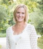 Smiling woman in a white sweater, standing outdoors with a blurred green background.
