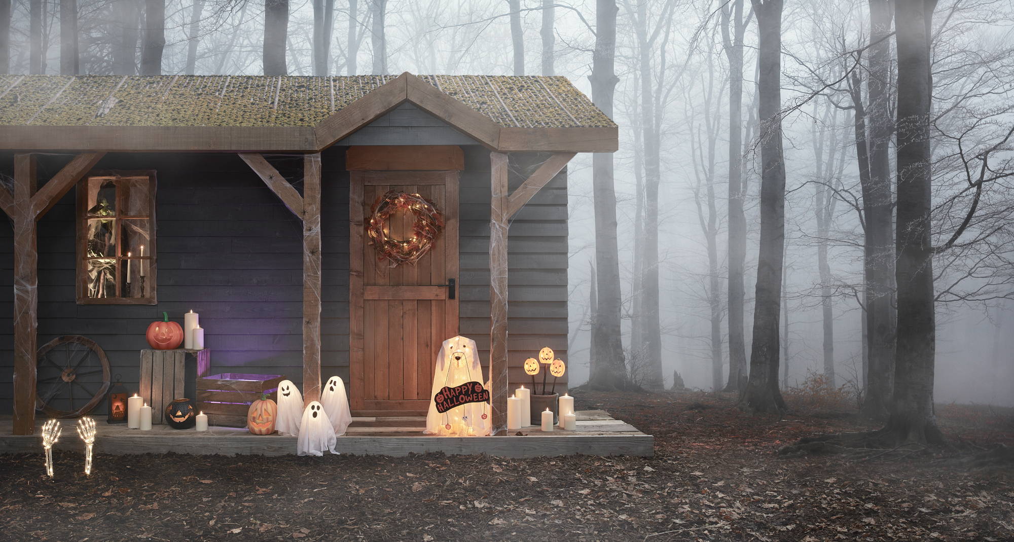 Eine Holzhütte im nebligen Wald mit einer mit einer Vielzahl von Halloween-Deko dekorierten Veranda