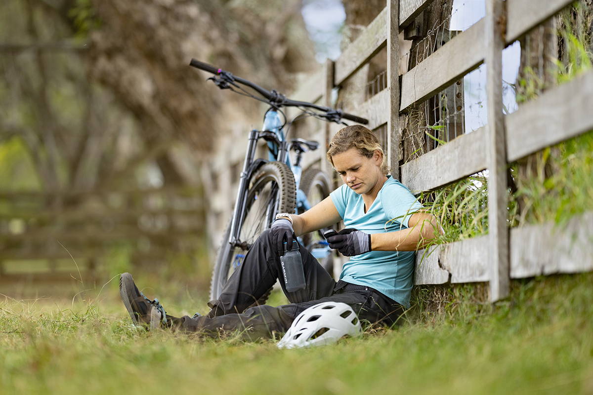 A cyclist relaxing against a wooden fence with her mountain bike while looking at her Garmin Edge 840 bike computer