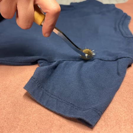 Tracing the shape of a T-shirt with a tracing wheel on a pattern piece