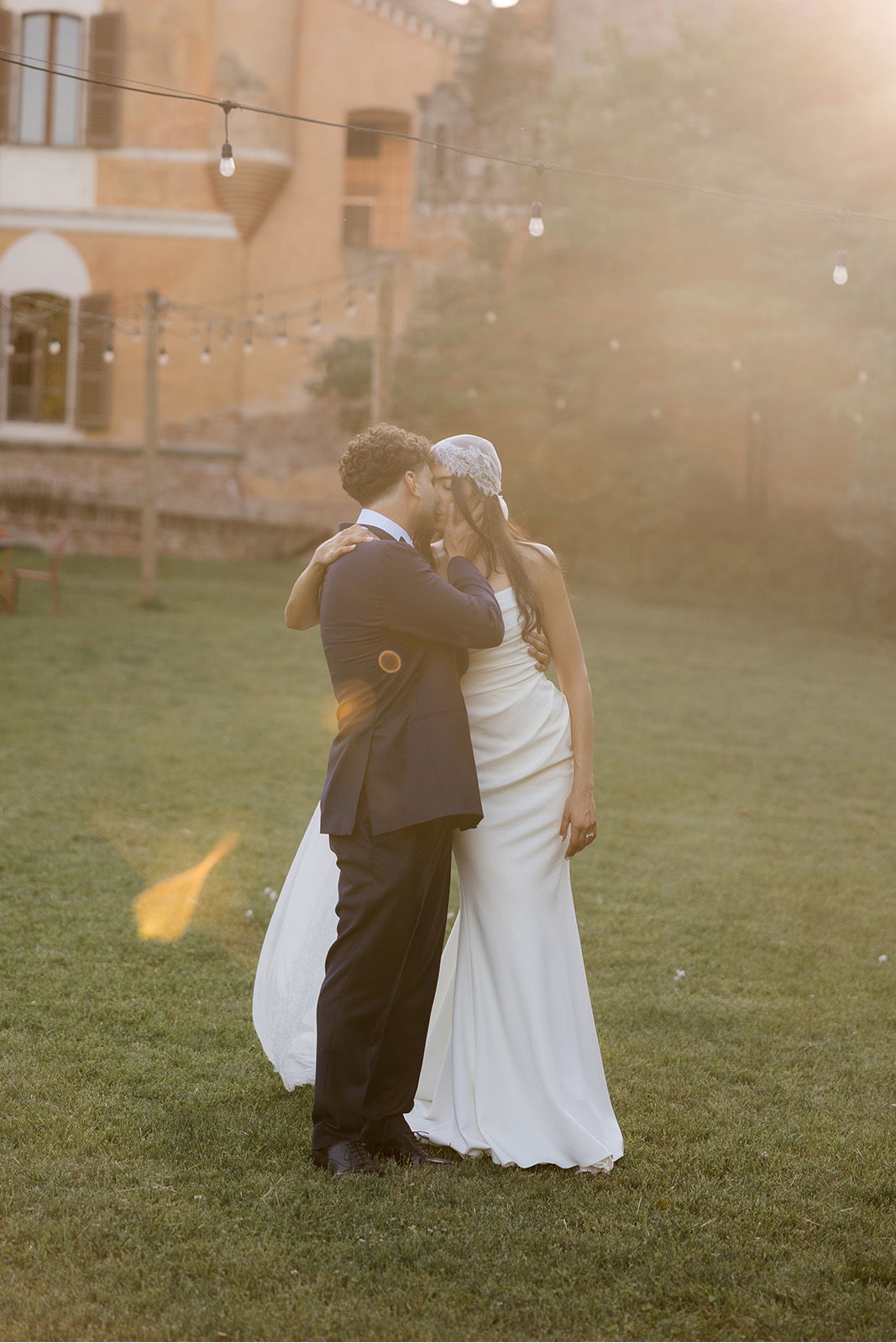 Couple embracing outdoors during a sunset, wearing wedding attire.