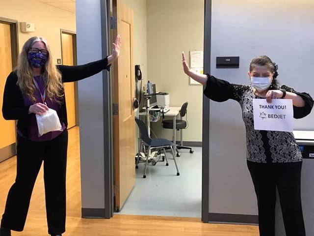 Two healthcare workers give a socially distanced high-five while holding a sign that says 