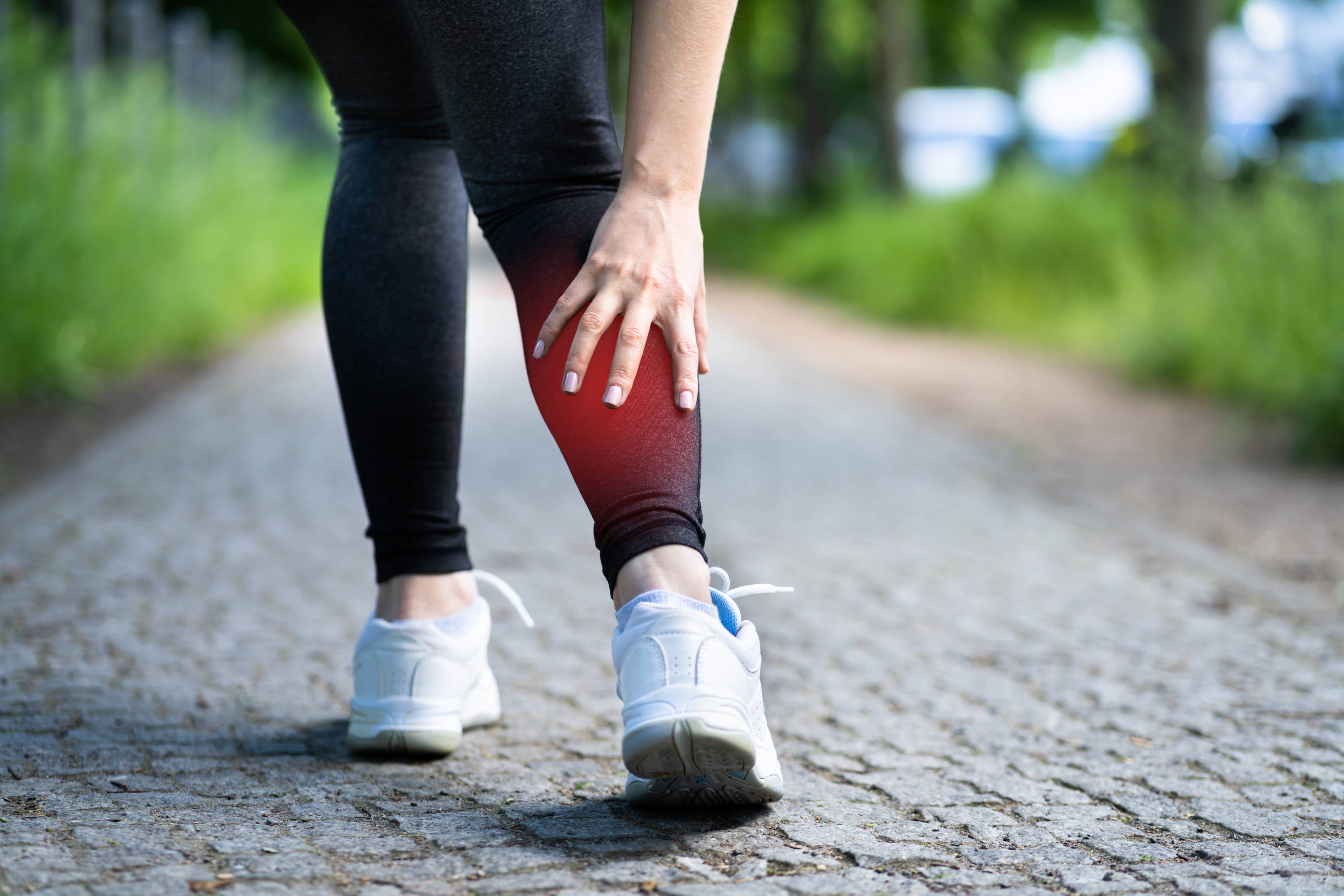 Woman grabbing leg in pain from swelling while walking outdoors