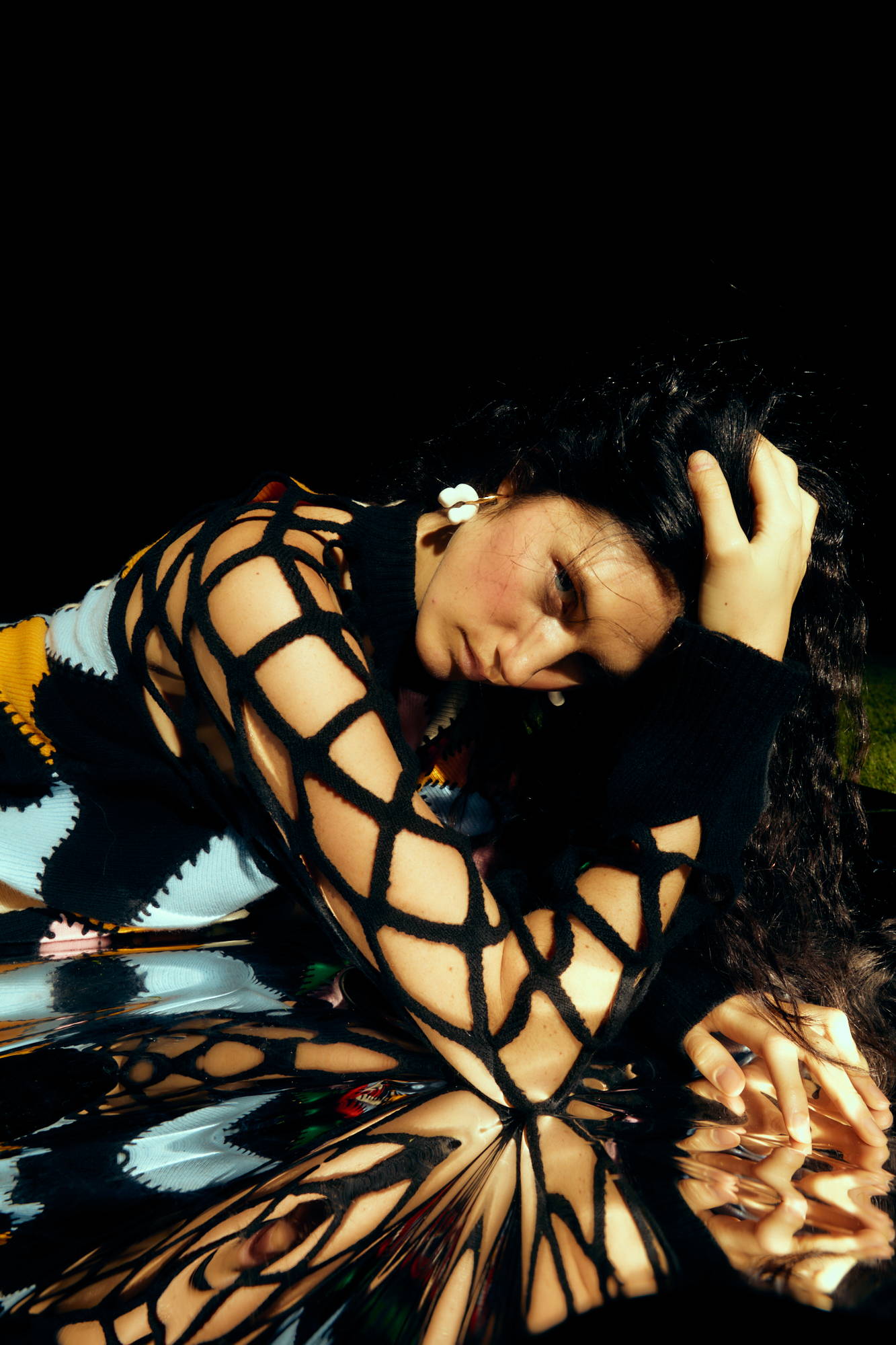 A person with long hair poses dramatically, wearing a patterned outfit.
