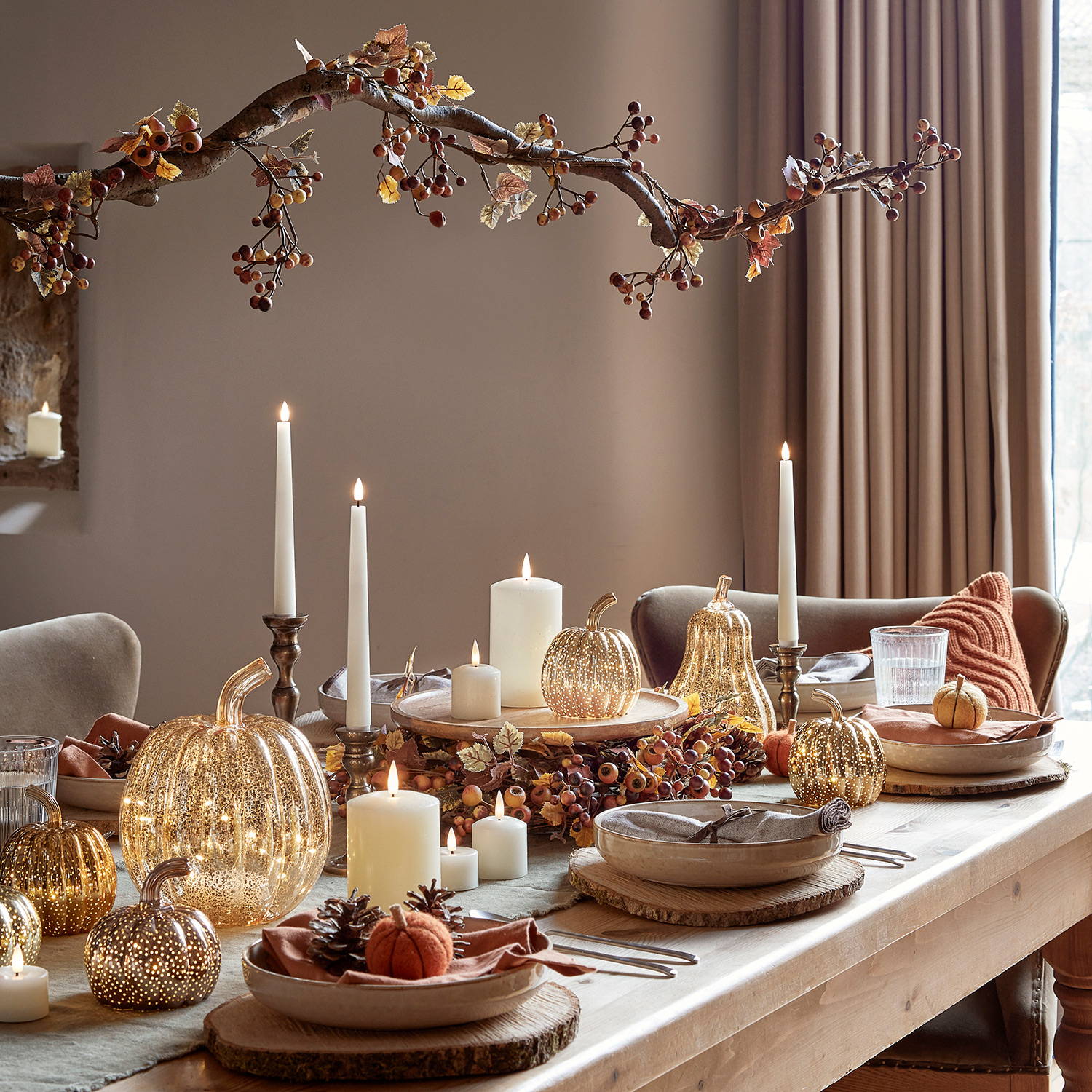 An autumn table with pumpkin lights, LED candles, a garland and mini pumpkins.