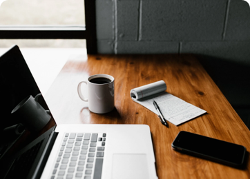 Laptop, coffee, pad and pen, and phone