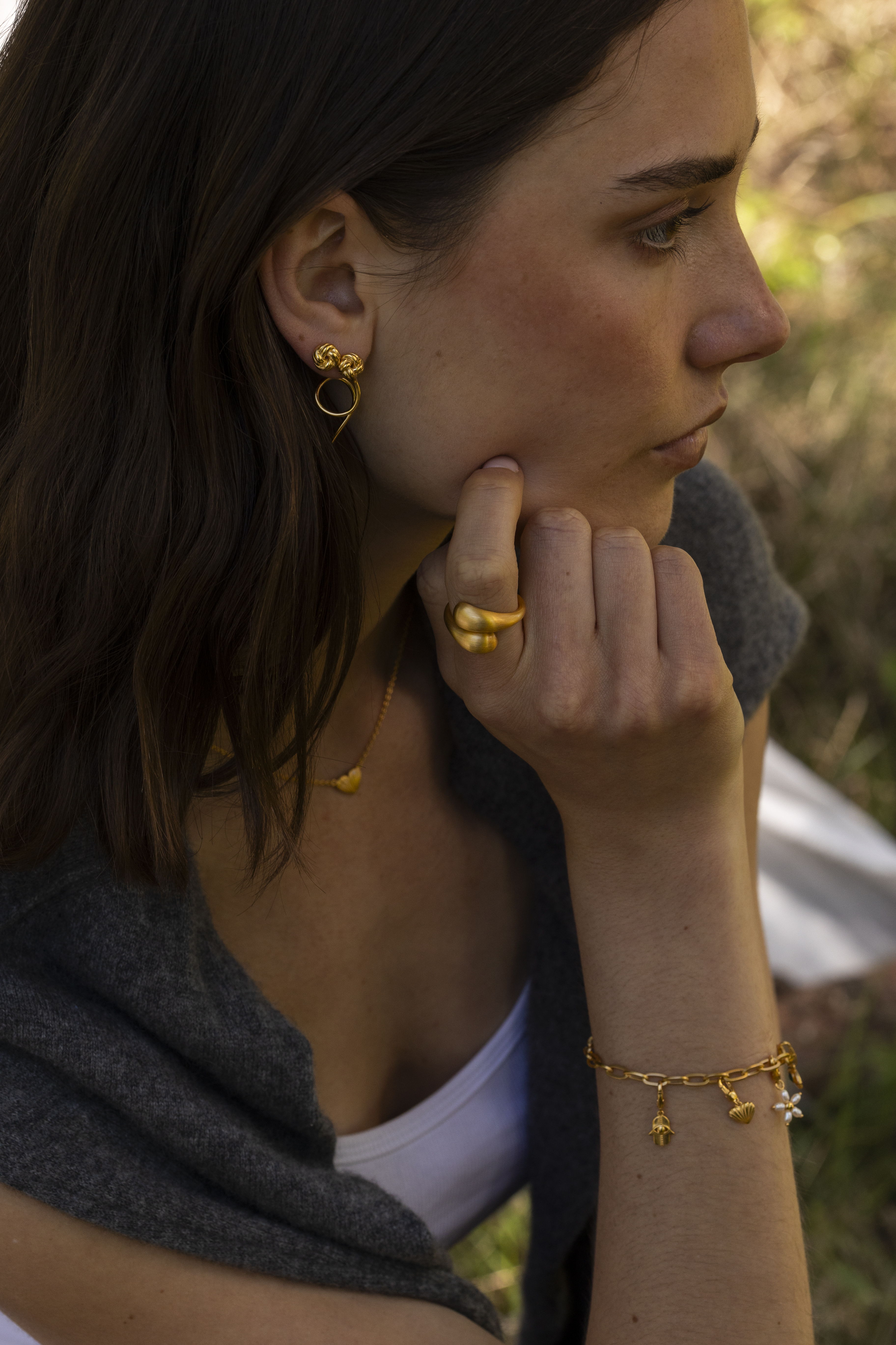 A woman wearing gold jewelry, resting her chin on her hand.