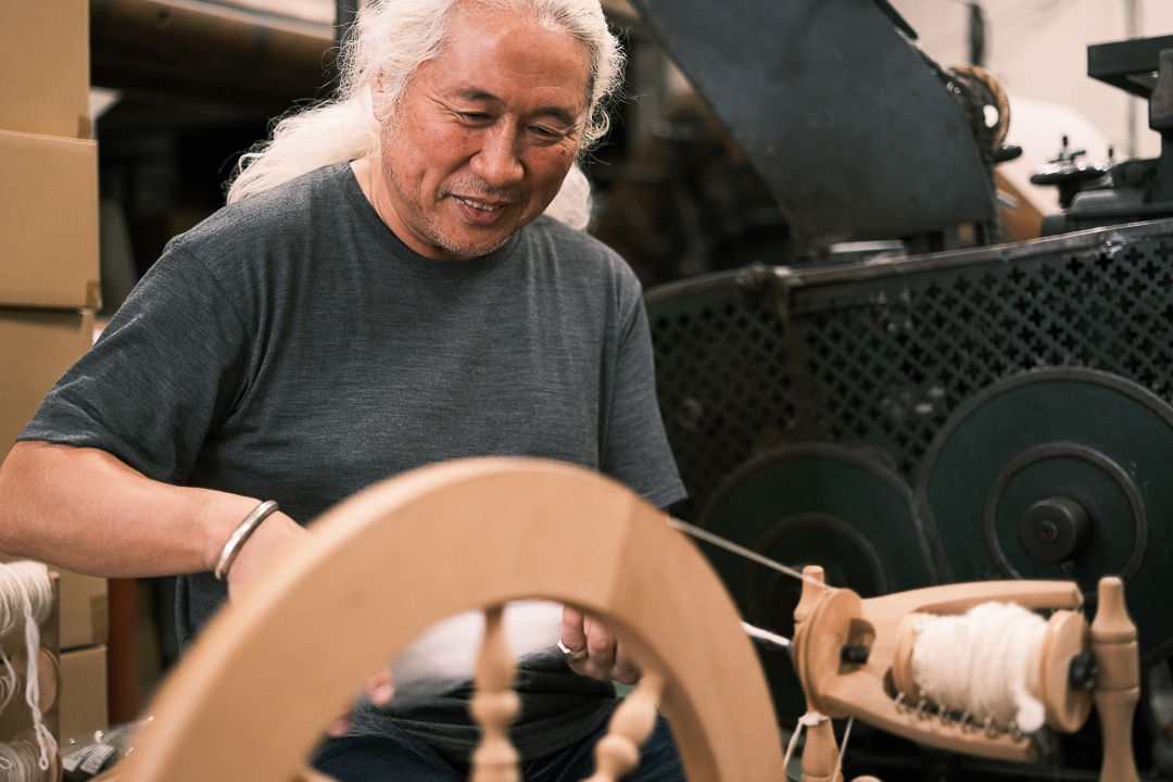 Person spinning yarn on a spinning wheel in a workshop setting.