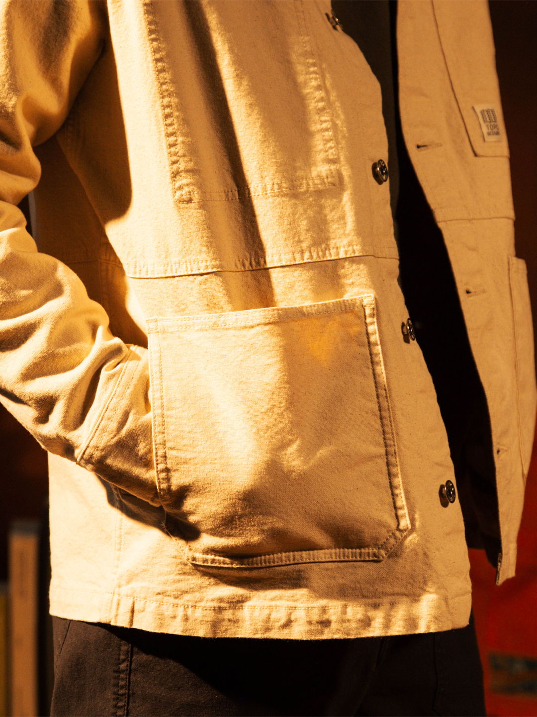 Person wearing a light beige jacket with a pocket, hands in pockets.