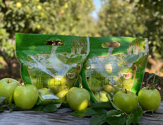 Two bags of green apples with some apples and leaves in the foreground.