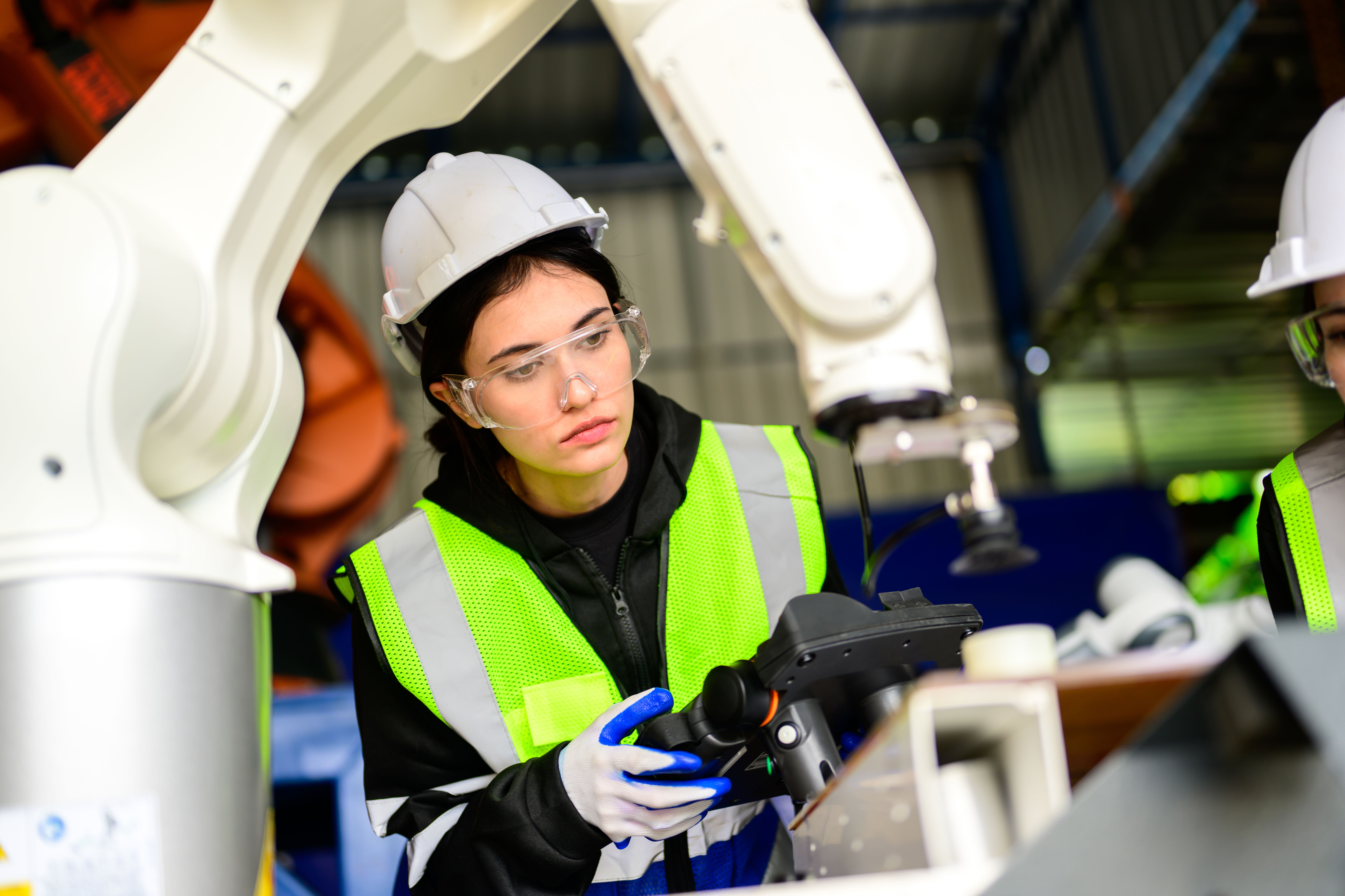 Worker wears safety vest and hard hat working with robotic arm