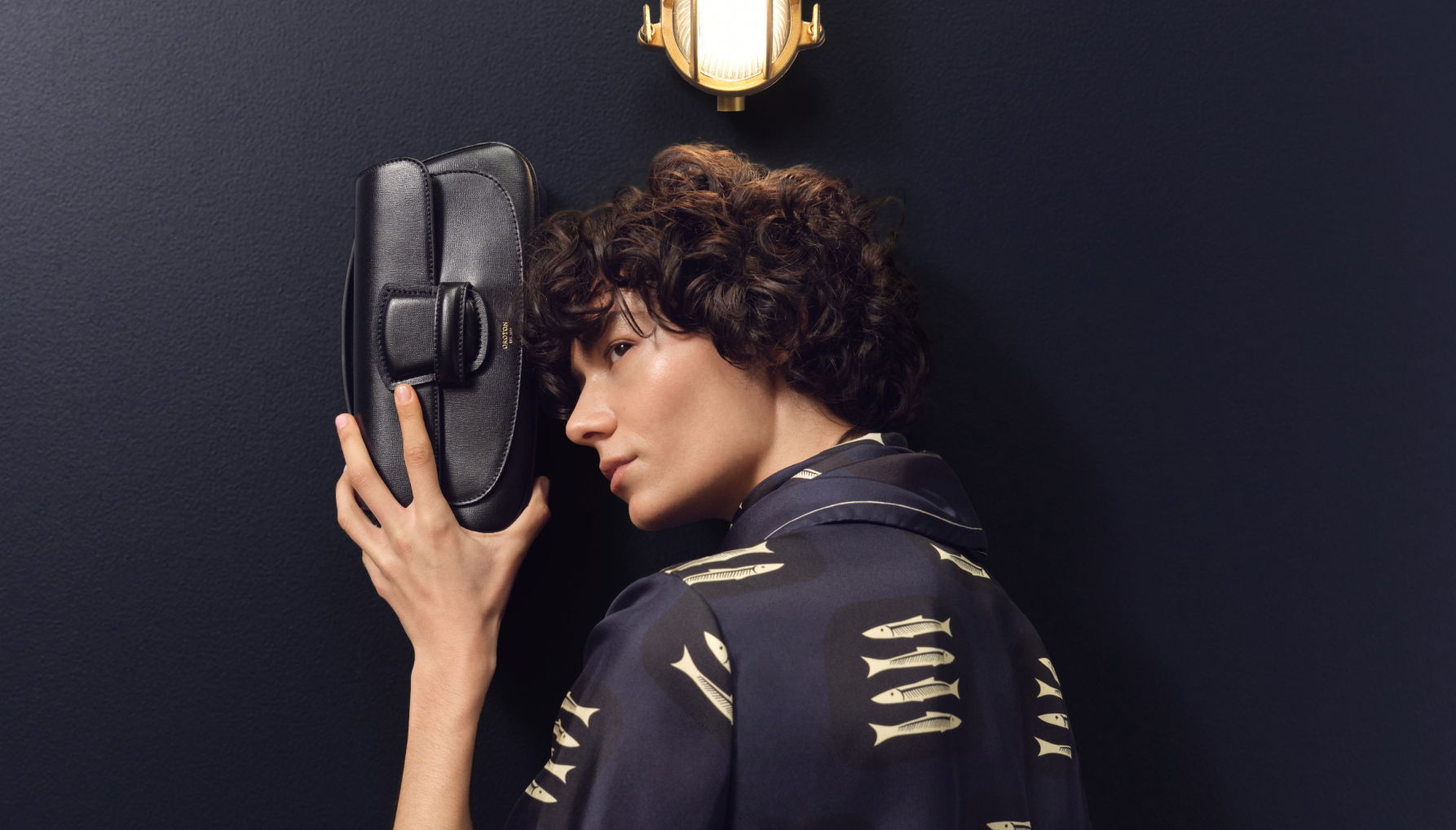 Person holding a black shoe against a dark background.