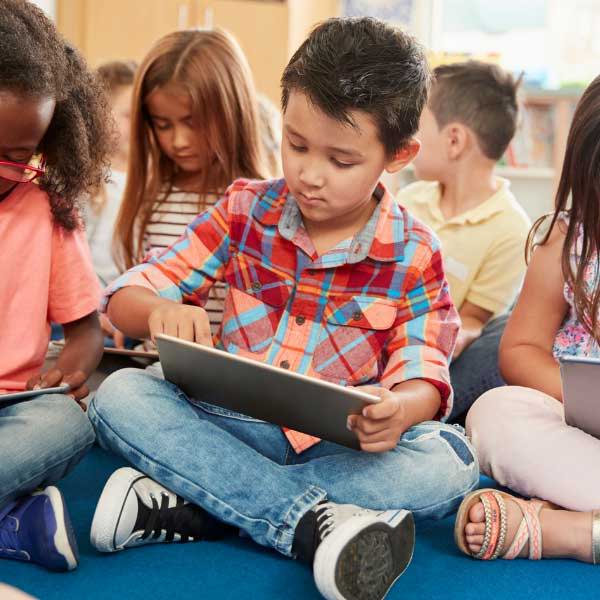 A group of school children on tablets sitting cross legged on the floor