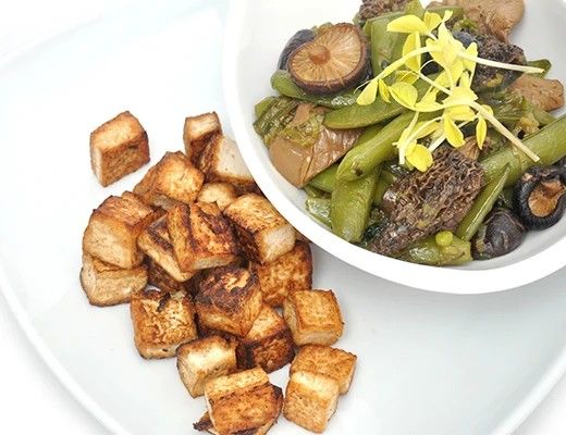 Bowl of mixed vegetables with tofu cubes on a white plate.