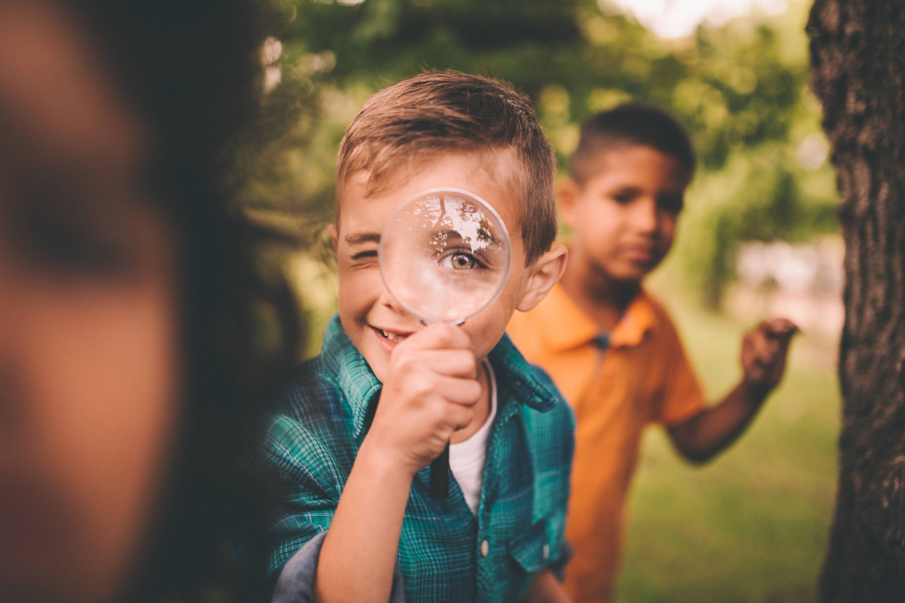 Barn leker utendørs – en gutt holder et forstørrelsesglass opp til øyet slik at det blir veldig stort, som en gal vitenskapsmann
