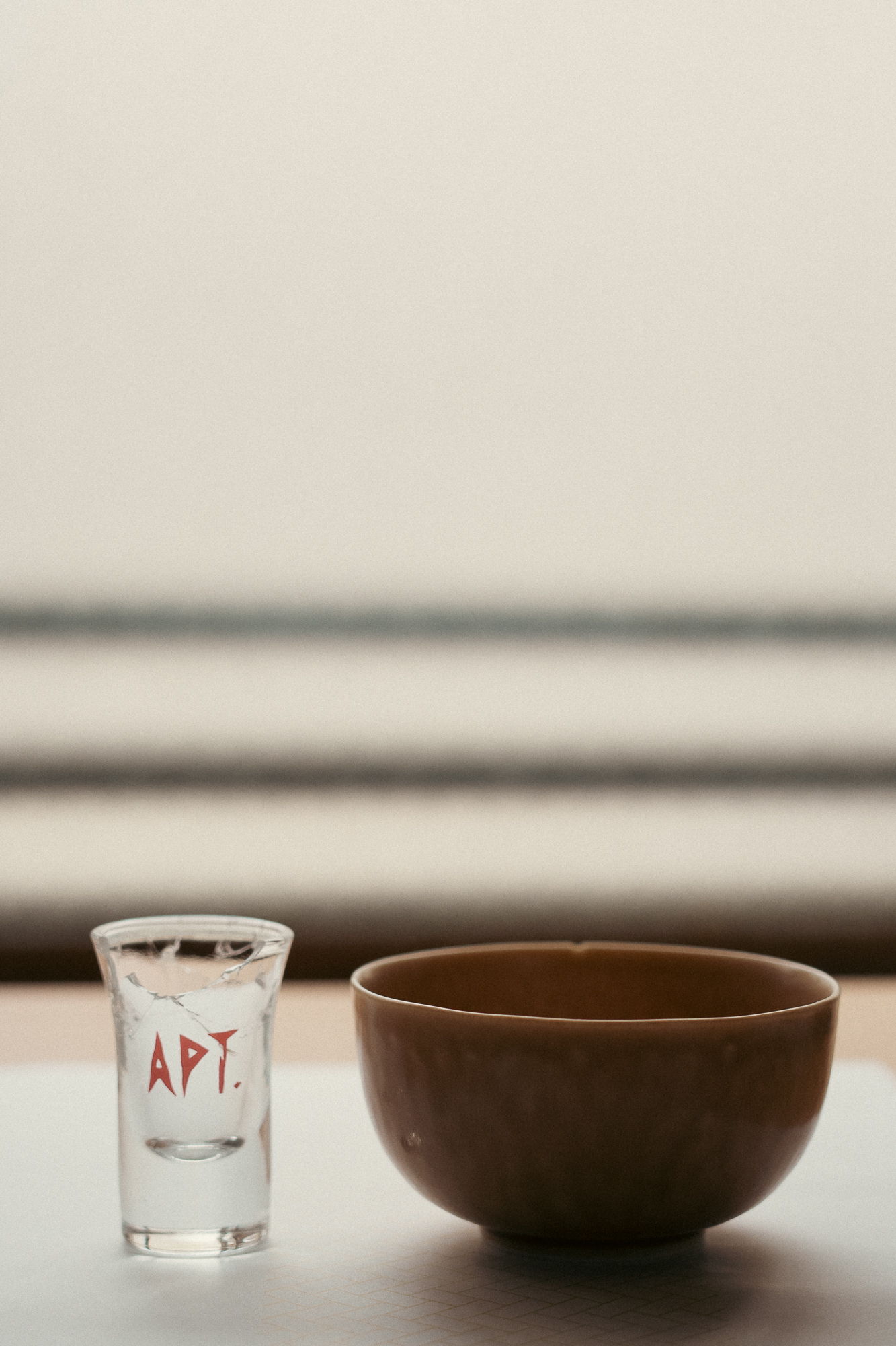 A shot glass and a brown bowl on a table.