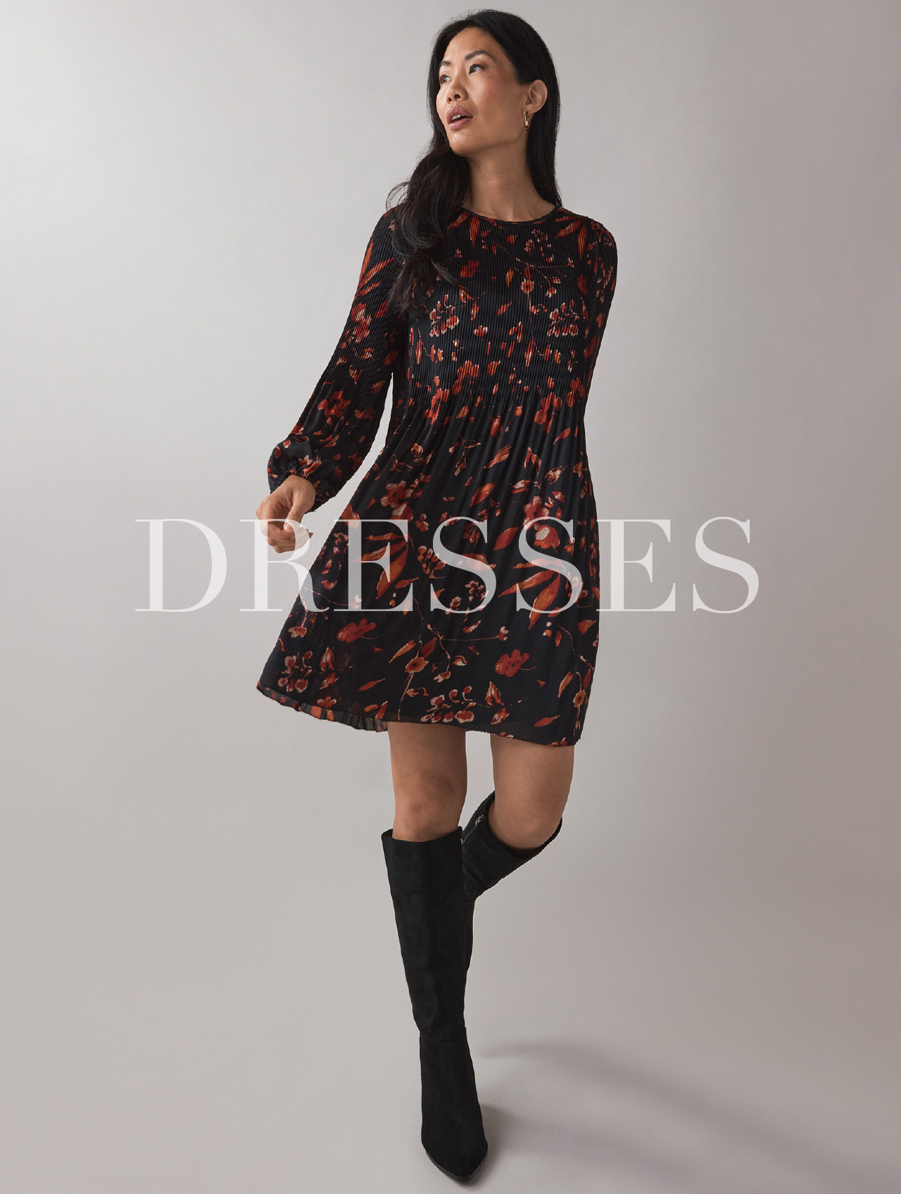 Woman wearing a floral dress and knee-high boots, standing against a neutral background.