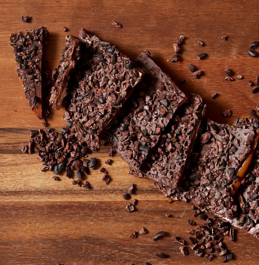 Sliced chocolate bar with cocoa nibs on a wooden surface.