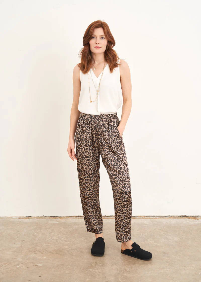 A model wearing a sleeveless off white v neck top with leopard print satin trousers and black clogs