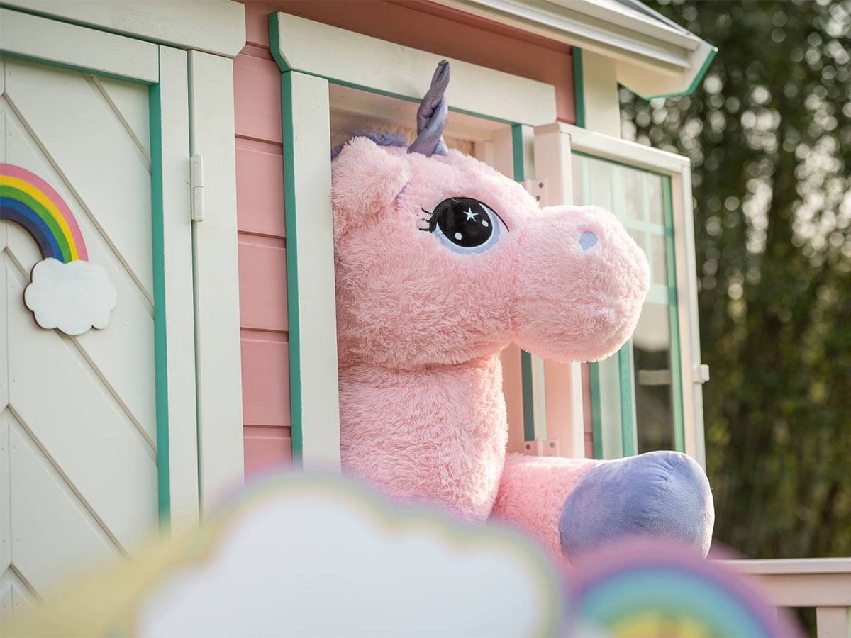 A unicorn looks out of a pink wooden playhouse window by WholeWoodPlayhouses