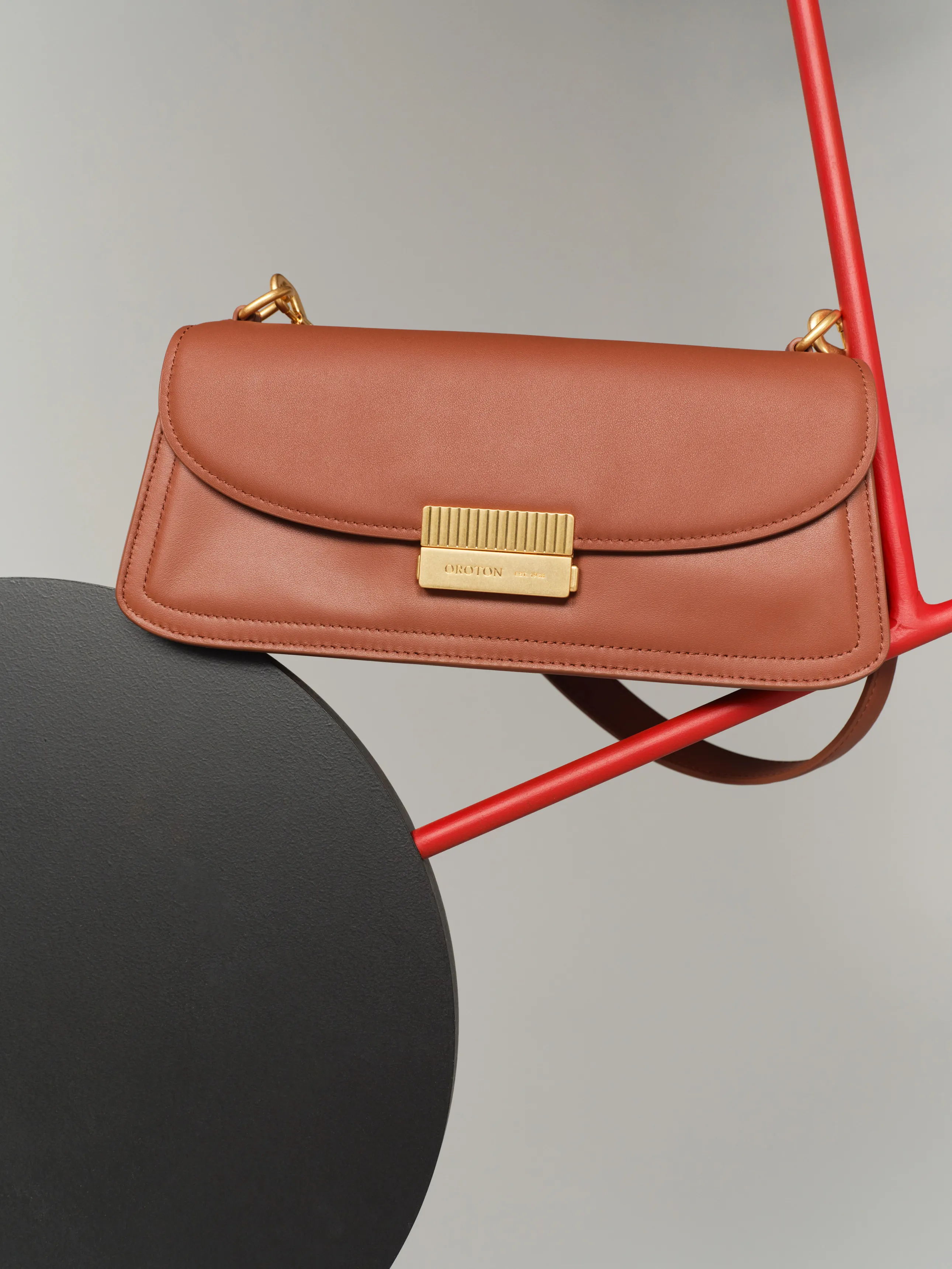 A brown leather handbag with a gold clasp on a red background.
