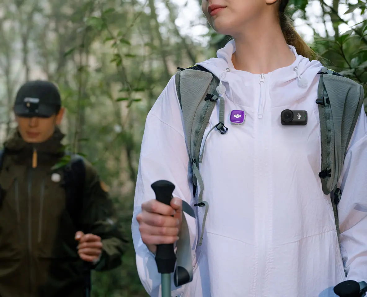 Two hikers in a forest, one wearing a white jacket and a DJI Osmo Nano camera.