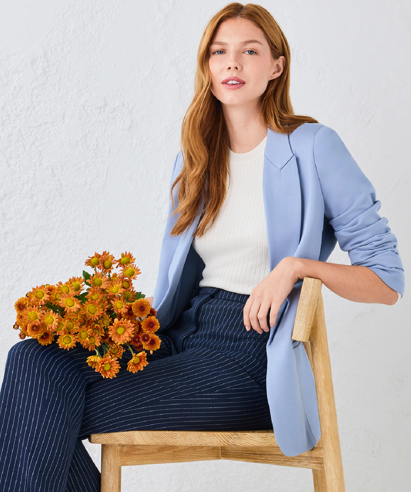 Woman in a blue blazer sitting with a bouquet of orange flowers.