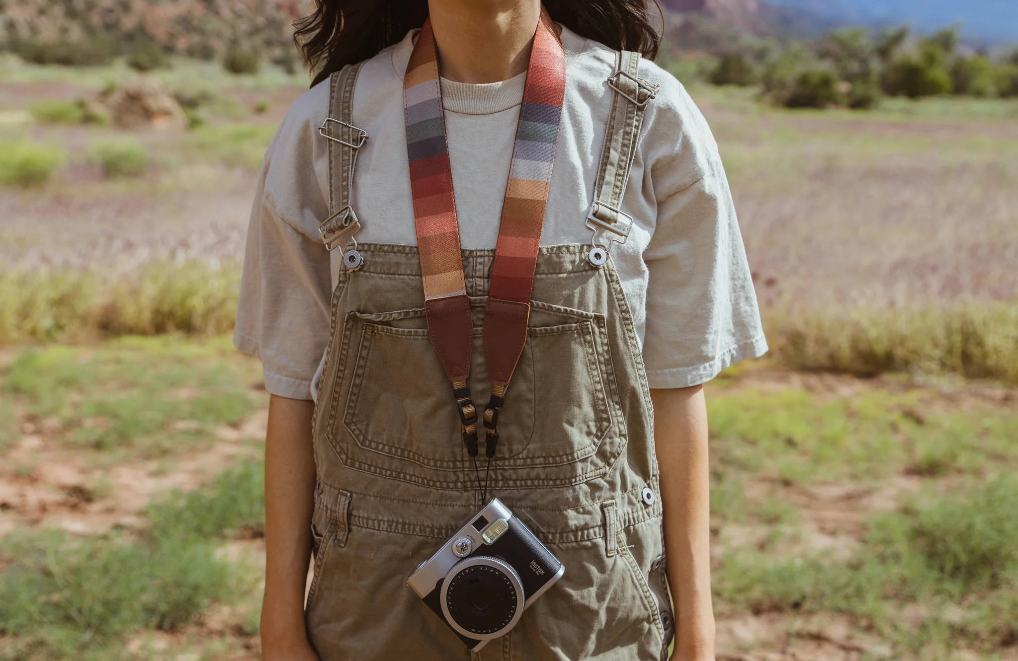 Girl wearing retro striped camera strap and overalls outside.