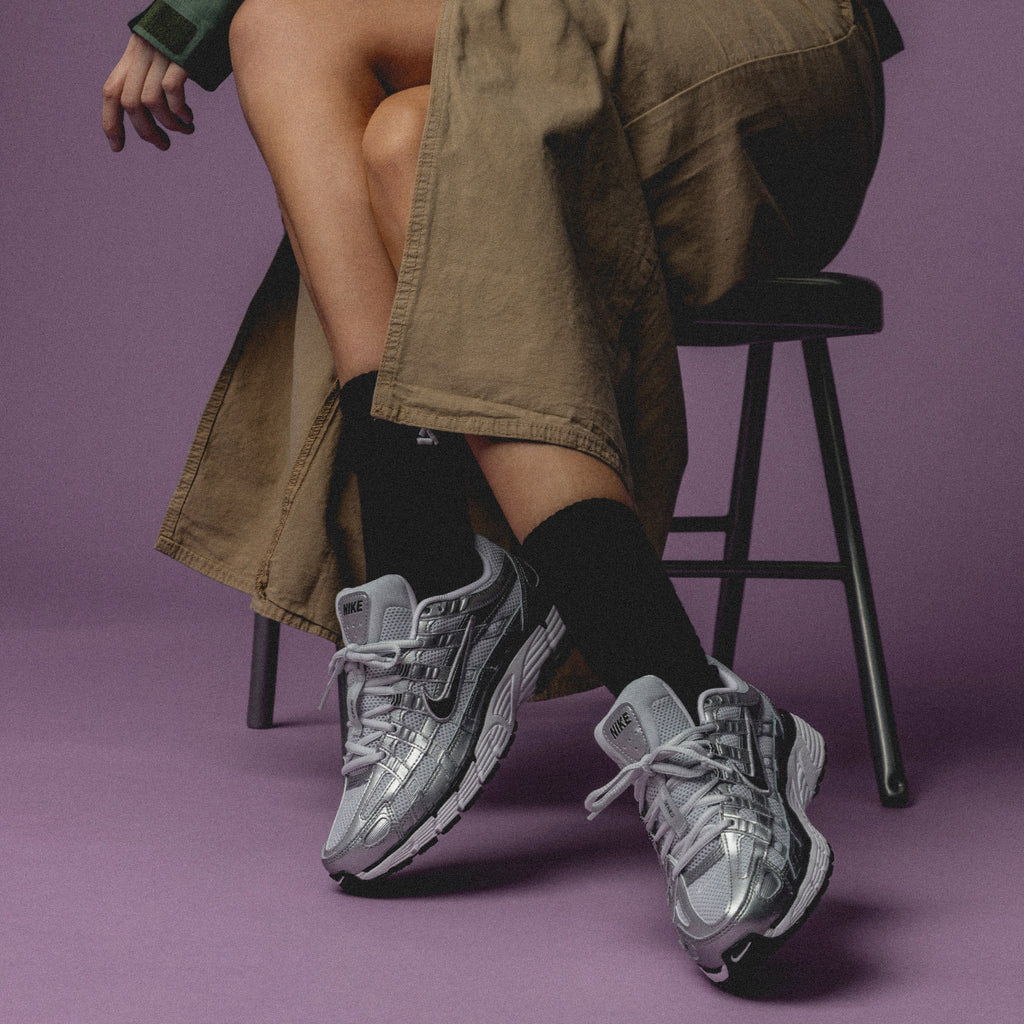Person sitting on a stool wearing stylish sneakers and long pants.