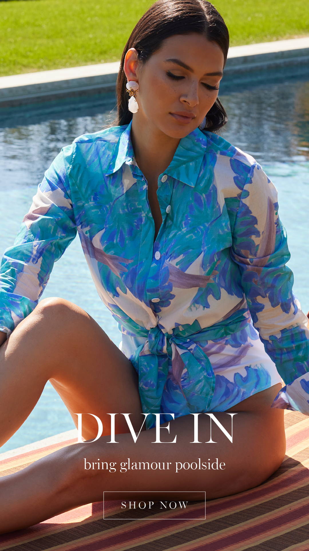 DIVE IN | bring glamour poolside | Woman sitting poolside wearing blue floral printed swimsuit with matching cotton shirt | Shop Now