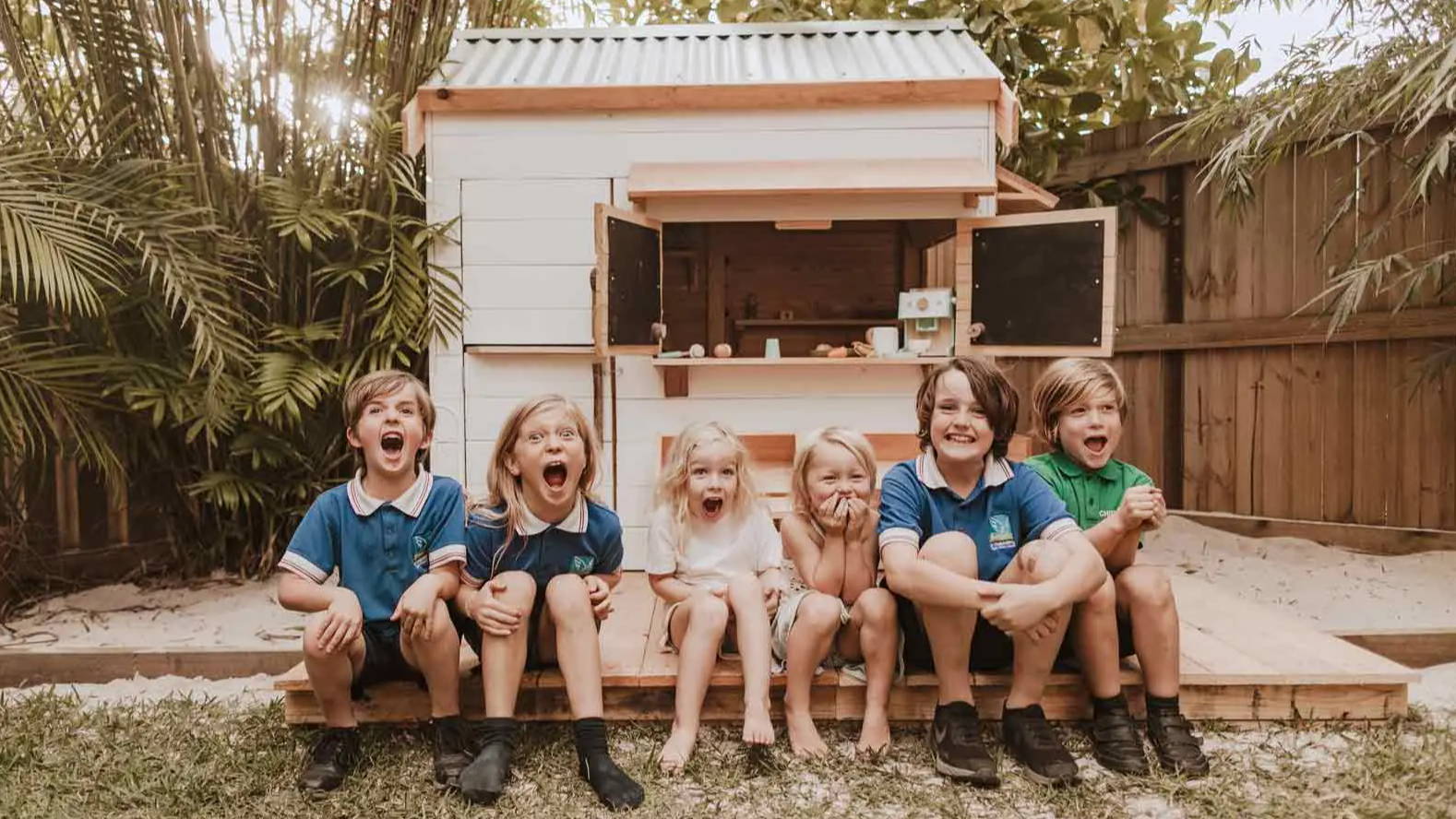 Children are smiling while sitting in front of a cubby house