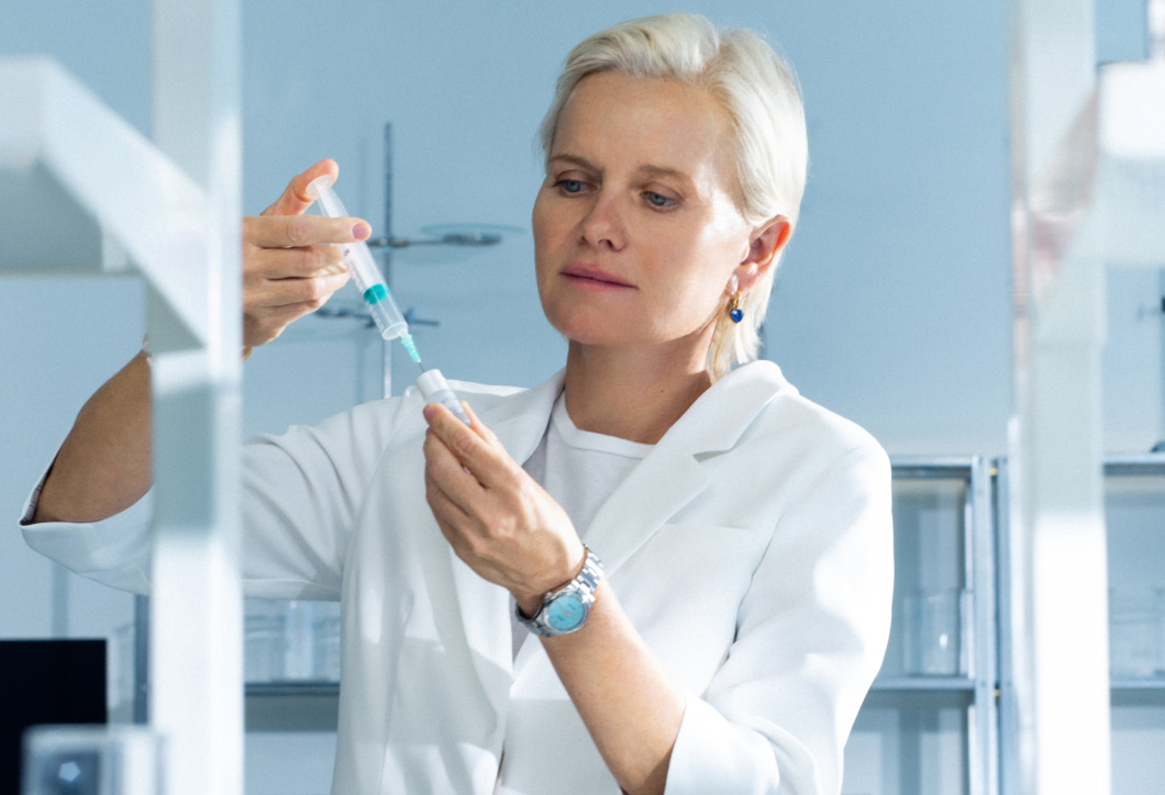 Woman in lab coat holding a syringe in a laboratory setting.