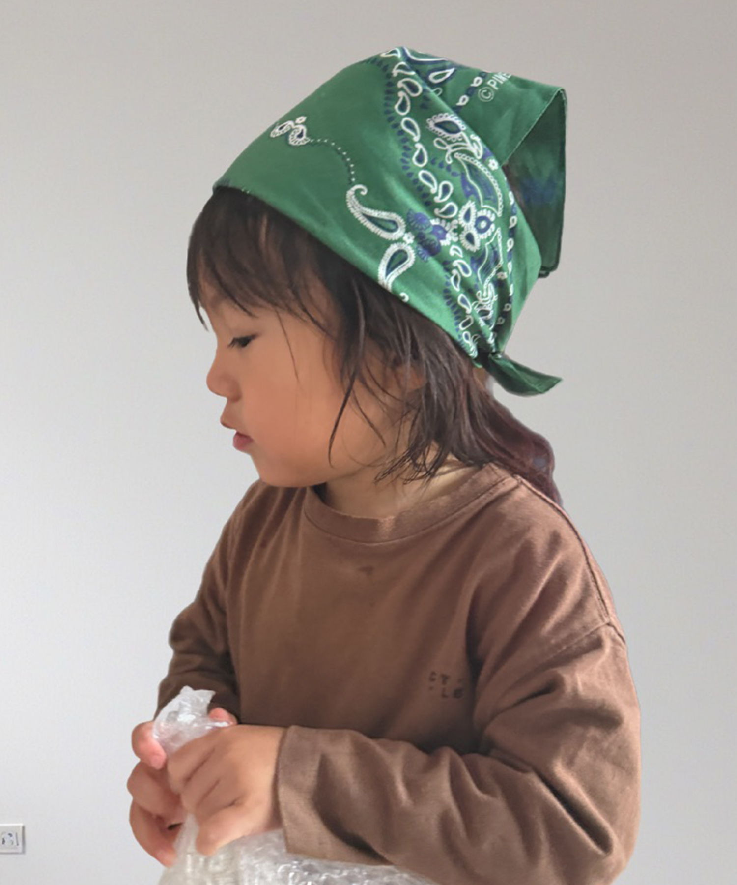 Child wearing a green bandana and brown shirt, looking to the side.