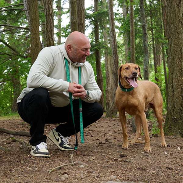 A person squatting next to a dog in a forested area.