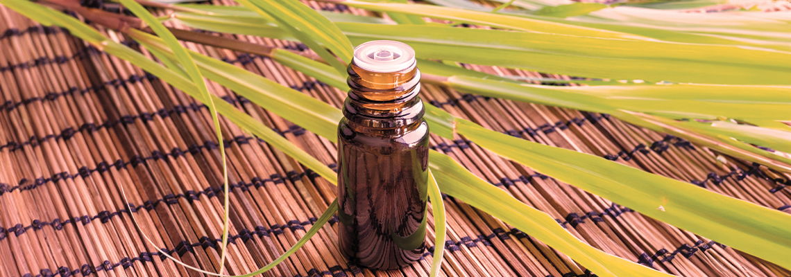 Brown essential oil bottle on a woven mat with green leaves.