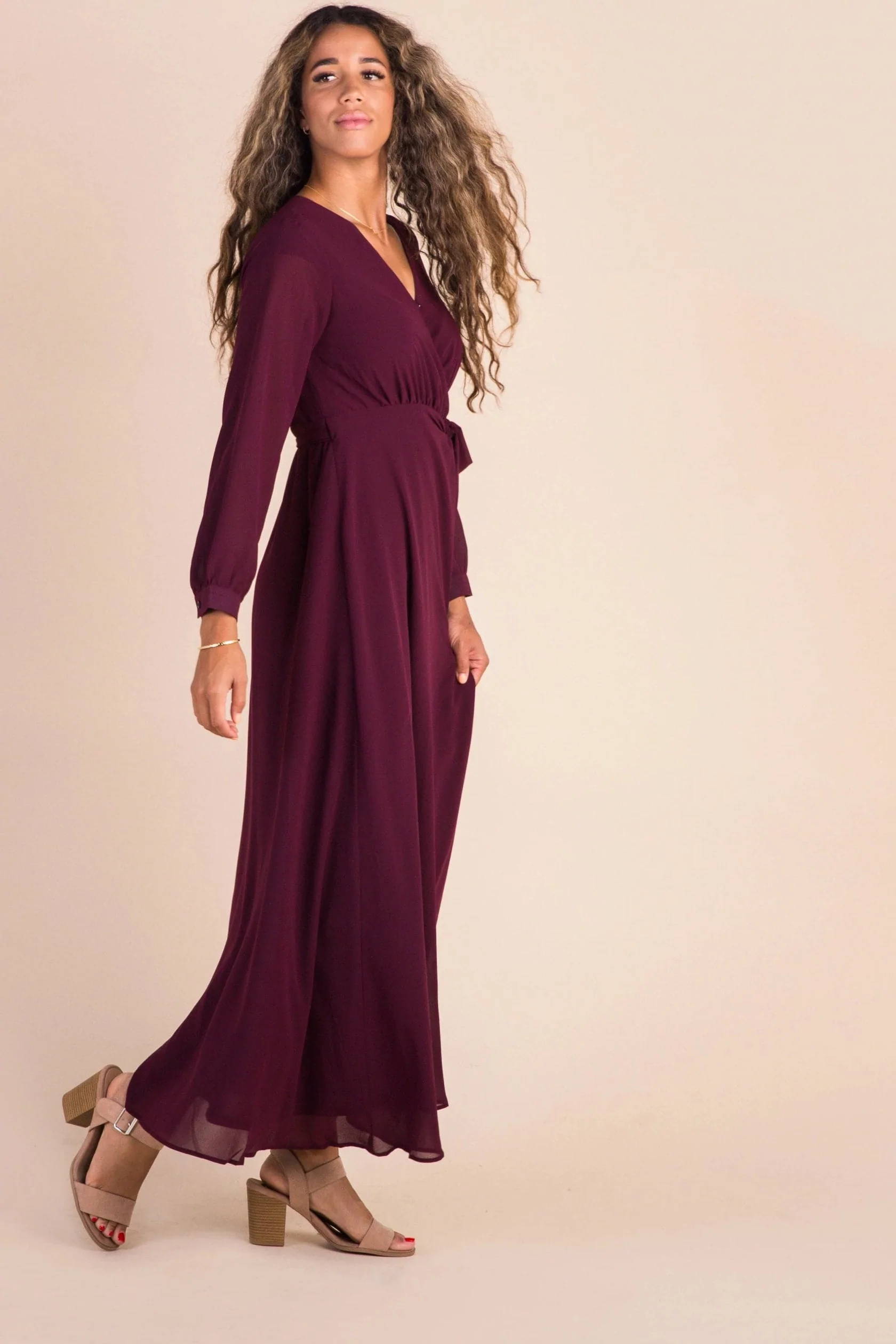  A woman poses in a dark red floor-length fall dress