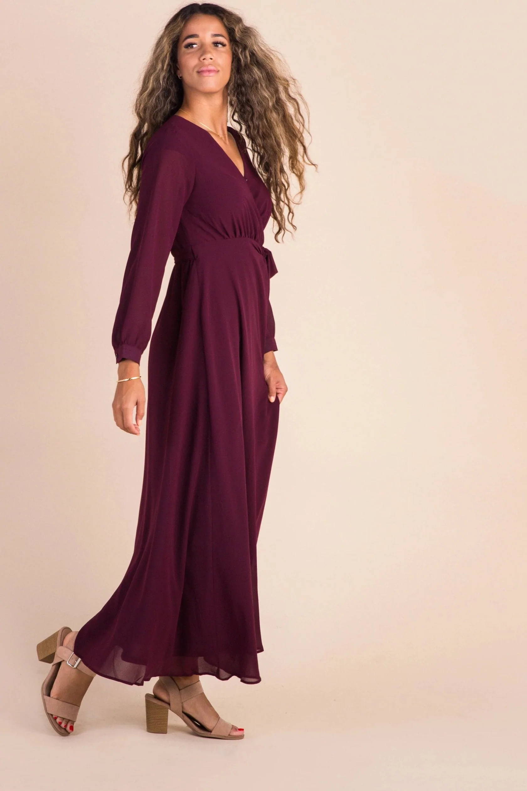 A woman poses in a dark red floor-length fall dress
