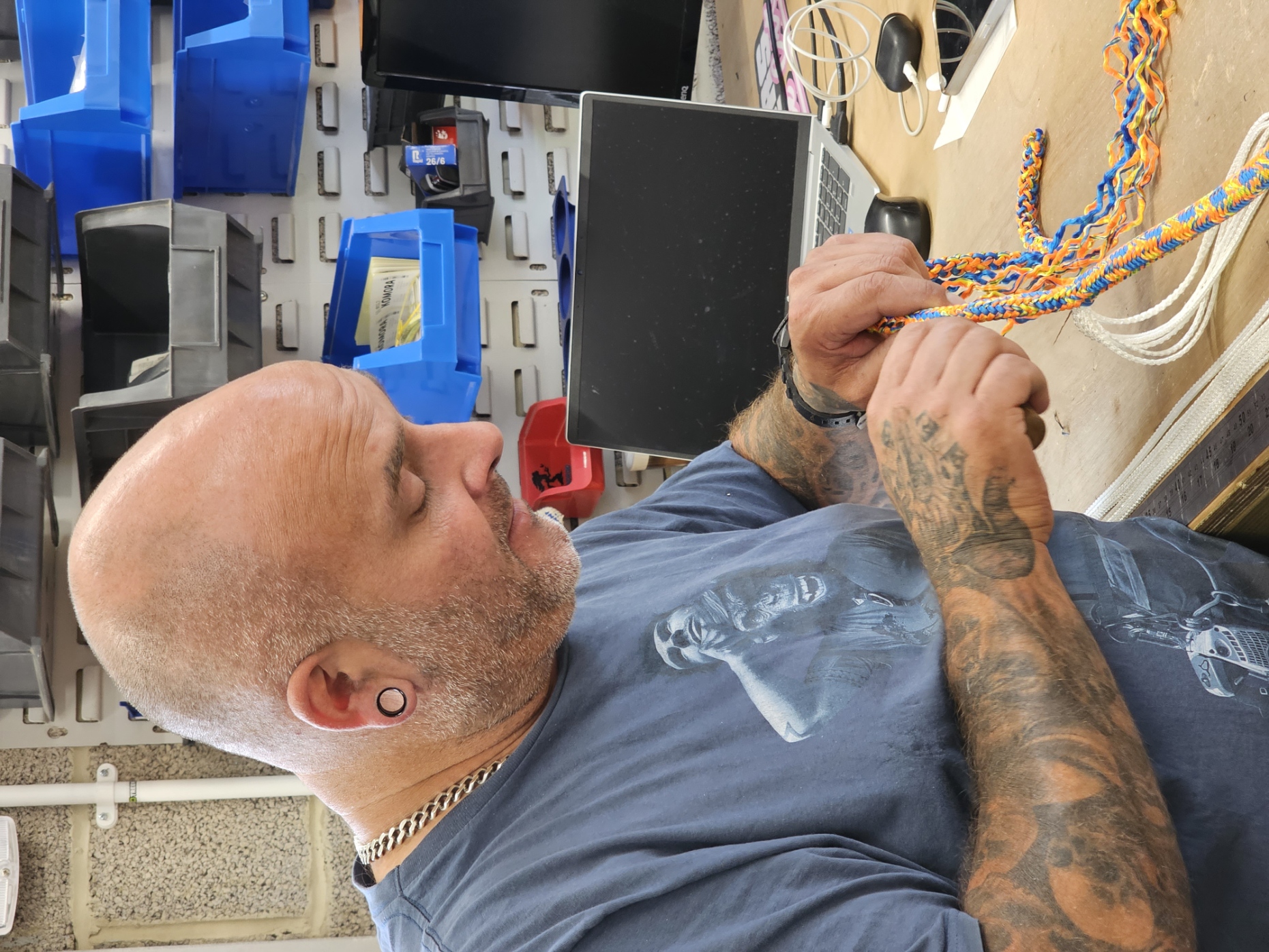 Man with tattoos working on colorful cords in a workshop.