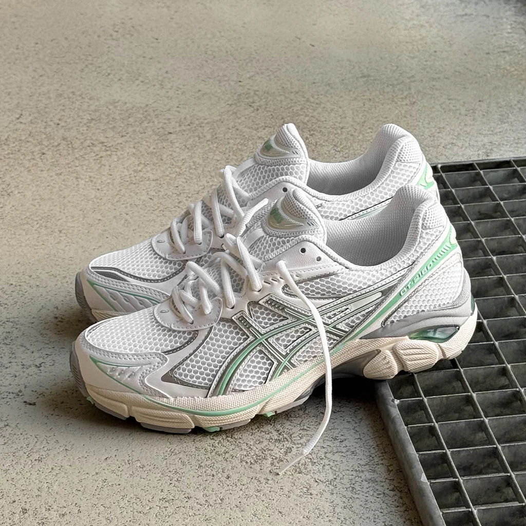 White athletic shoes with green accents on a textured surface.