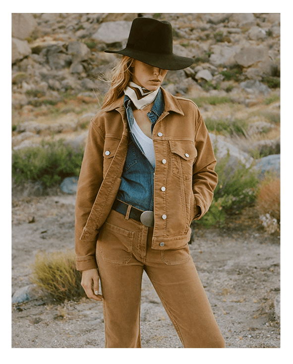 Woman in brown outfit and hat standing in a rocky landscape.