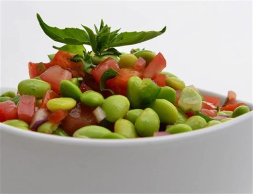 Bowl of fresh salad with tomatoes, edamame, and a mint garnish.