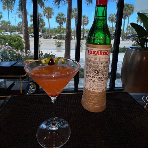 A cocktail with a Luxardo bottle and palm trees in the background.