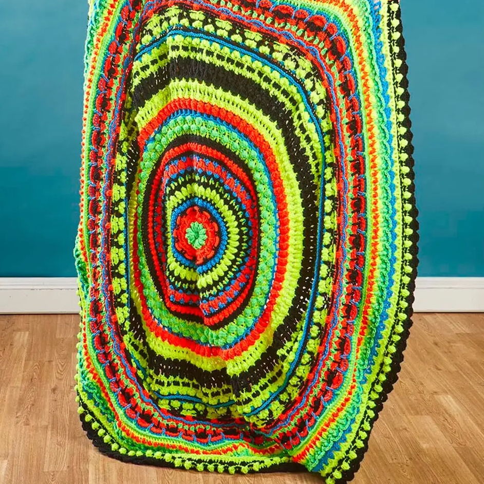 Colorful, circular crochet blanket displayed against a blue wall.