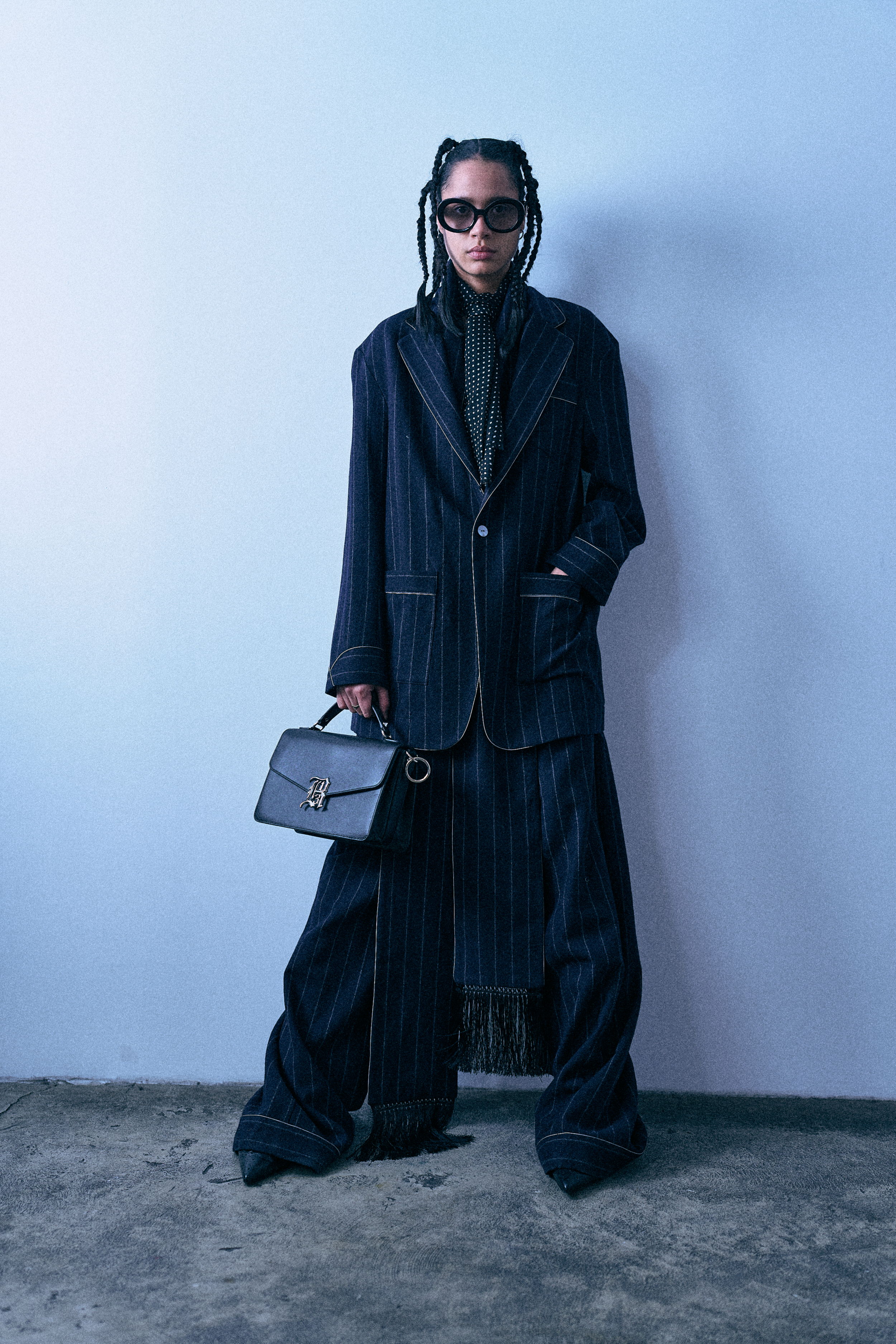 Person wearing oversized pinstripe suit holding a handbag against a blue background.