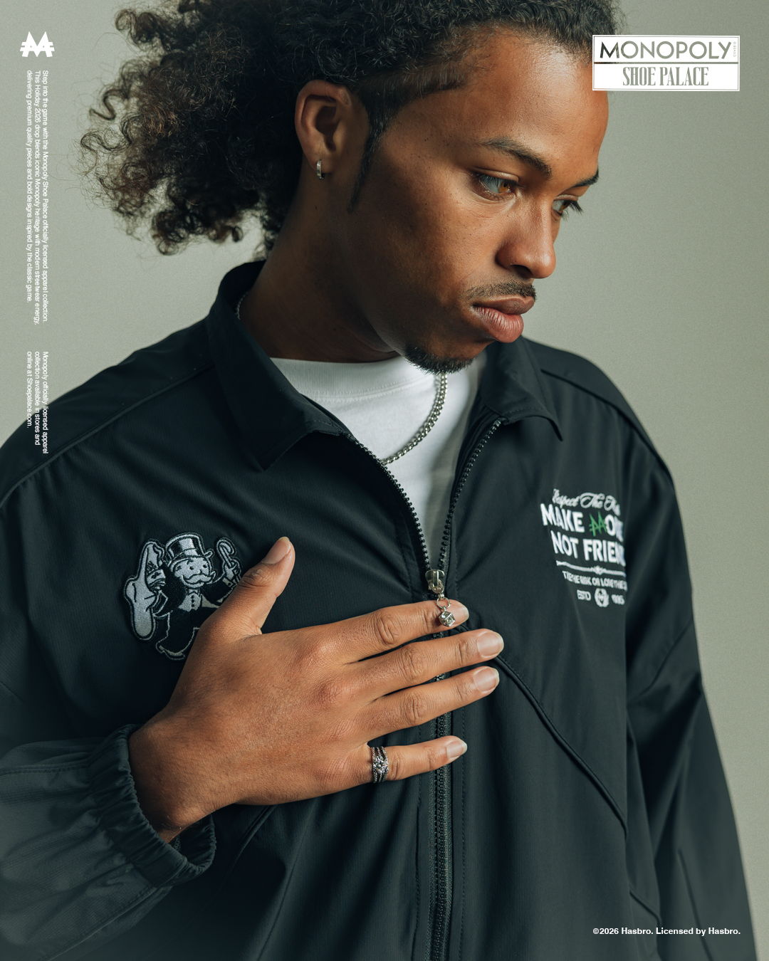 A man in a black jacket with curly hair, looking thoughtfully, hand on chest.