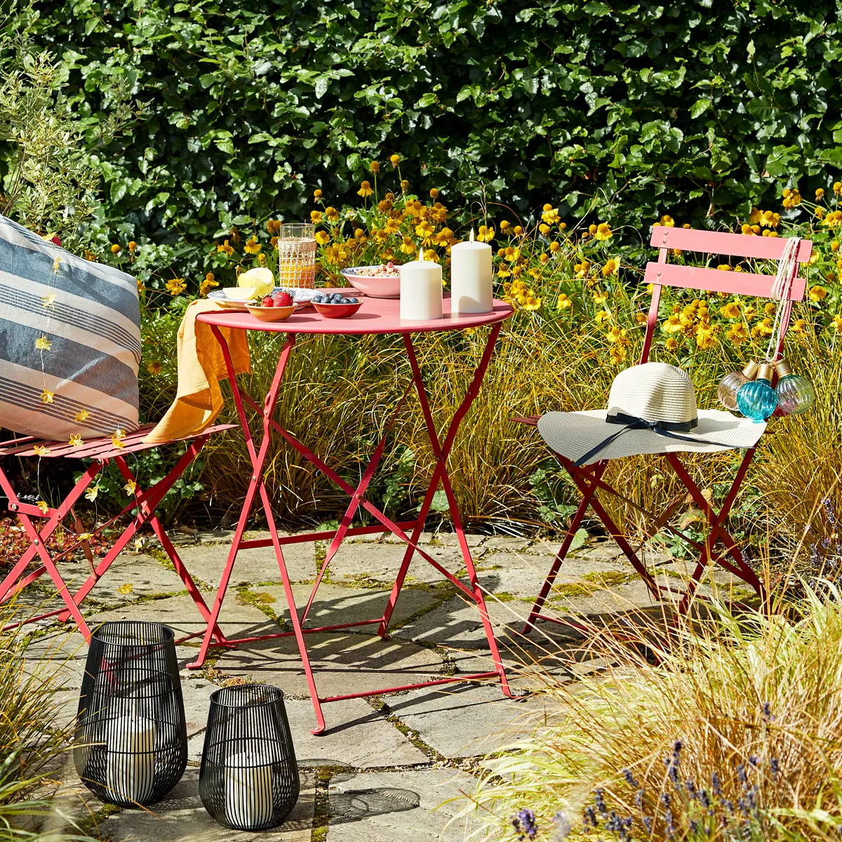 Garden picnic area with red bistro set, featuring colourful hanging lights, lanterns and LED candles