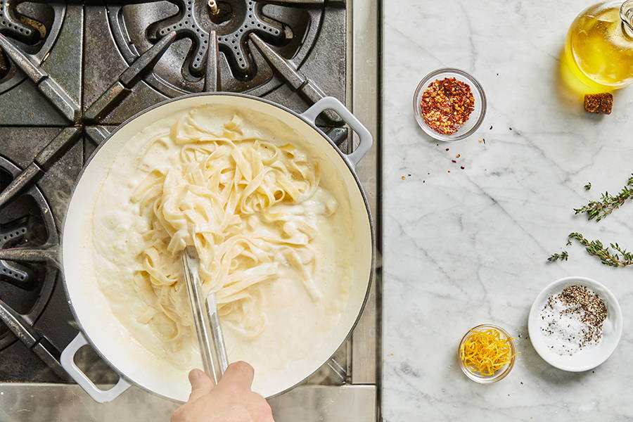 Pasta being combined with sauce using tongs.