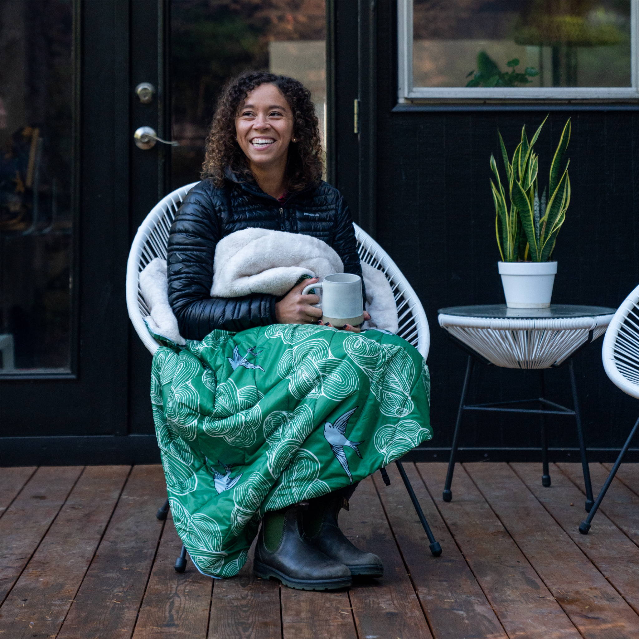 Woman smiling wrapped in blanket sitting on chair on porch