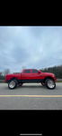 Side profile of lifted red RAM 1500 with chrome wheels and off-road tires on rural road